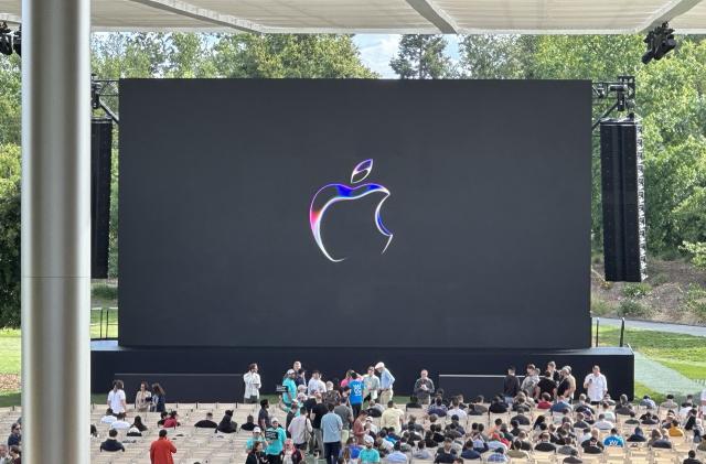 The Apple logo on a black screen with a stage and rows of seats in front of it.