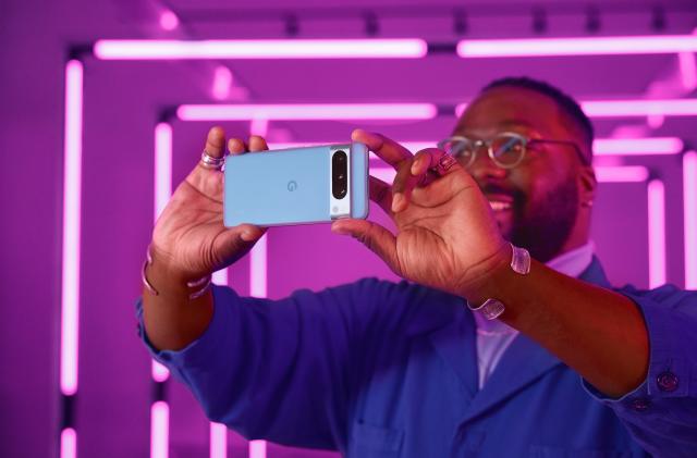 A person takes a photo with a horizontally orientated Google Pixel 8 Pro. Purple light tubes illuminate the background.