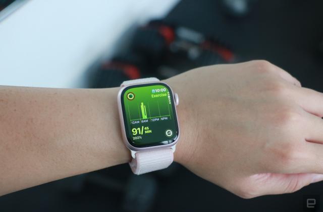The Apple Watch Series 9 on a person's wrist in front of some gym equipment, showing the Exercise page of the Move rings app.