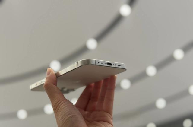 The iPhone 15 Pro Max held up against a ceiling of lights, showing its USB-C port.