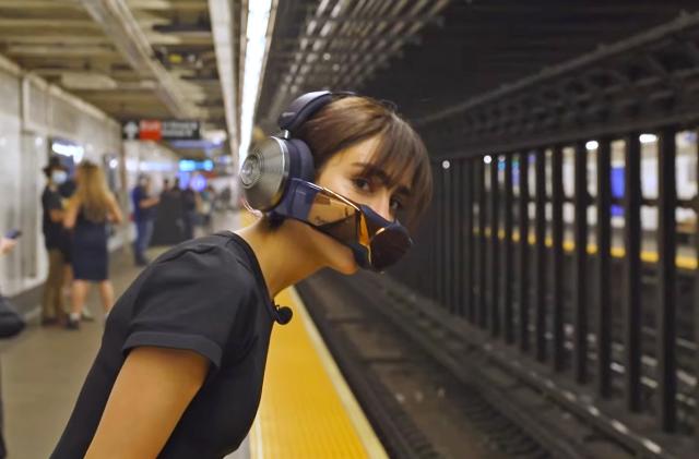 A young woman wearing the Dyson Zone headphones and breathing mask leans over the subway platform edge to see if a train is coming.